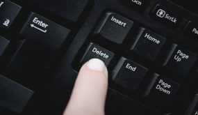 Finger over the delete key from a dusty black keyboard.