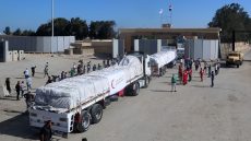 People on the Egyptian side of the Rafah border crossing watch as a convoy of lorries carrying humanitarian aid crosses to the Gaza Strip on October 21, 2023. The first of 20 trucks carrying humanitarian aid entered the war-torn and besieged Gaza Strip on October 21 through the Rafah border crossing with Egypt, said AFP correspondents on both sides. (Photo by Mohammed Assad / AFP)