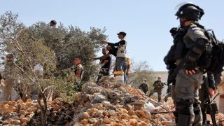 Israeli forces look on as Palestinian and foreign volunteers and activists pick olives next to the Israeli outpost of Evitar in solidarity with Palestinians whose land was confiscated by Israeli settlers, in the village of Beita, north of Nablus in the occupied West Bank, on October 10, 2021. (Photo by JAAFAR ASHTIYEH / AFP) (Photo by JAAFAR ASHTIYEH/AFP via Getty Images)