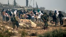 Israeli soldiers stand by as masked Israeli settlers throw stones at Palestinian protesters (unseen) gathering during a demonstration against construction on an Israeli outpost near the Palestinian village of Turmus Ayya and the Israeli settlement of Shilo, north of Ramallah in the occupied West Bank, on October 17, 2019. (Photo by JAAFAR ASHTIYEH / AFP) (Photo by JAAFAR ASHTIYEH/AFP via Getty Images)