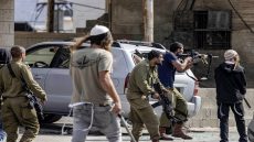 Israeli settlers fire at Palestinians (unseen) while an Israeli soldier (L) stands by during clashes in the town of Huwara in the occupied West Bank on October 13, 2022. (Photo by Oren ZIV / AFP)